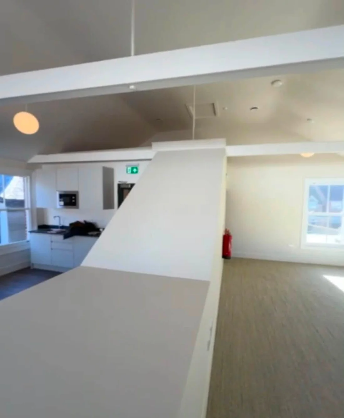 The shared kitchenette with white cabinets, a sink and microwave beside the central partition.