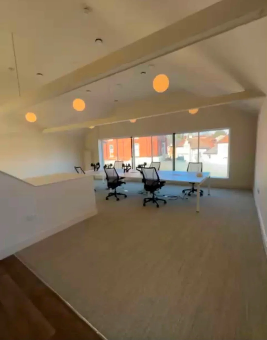 A wide view of the bright workspace, with open floor space, white beams and warm pendant lights.
